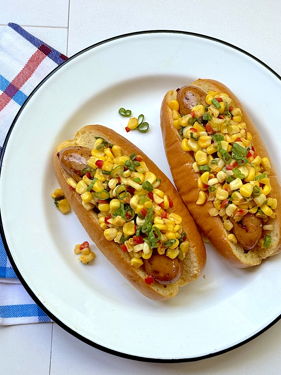 Two Melty Cheddar Chicken Sausage dogs with spicy corn relish.
